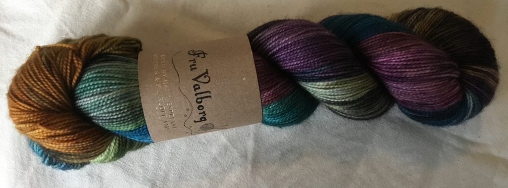 One skein Fru Valborg yarn in a deep purple, green and brown multi color