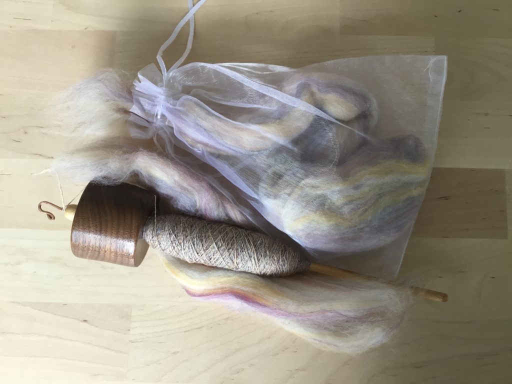 Top whorl spindle with pale yellow and purple singles on the cop and a handful of fiber attached