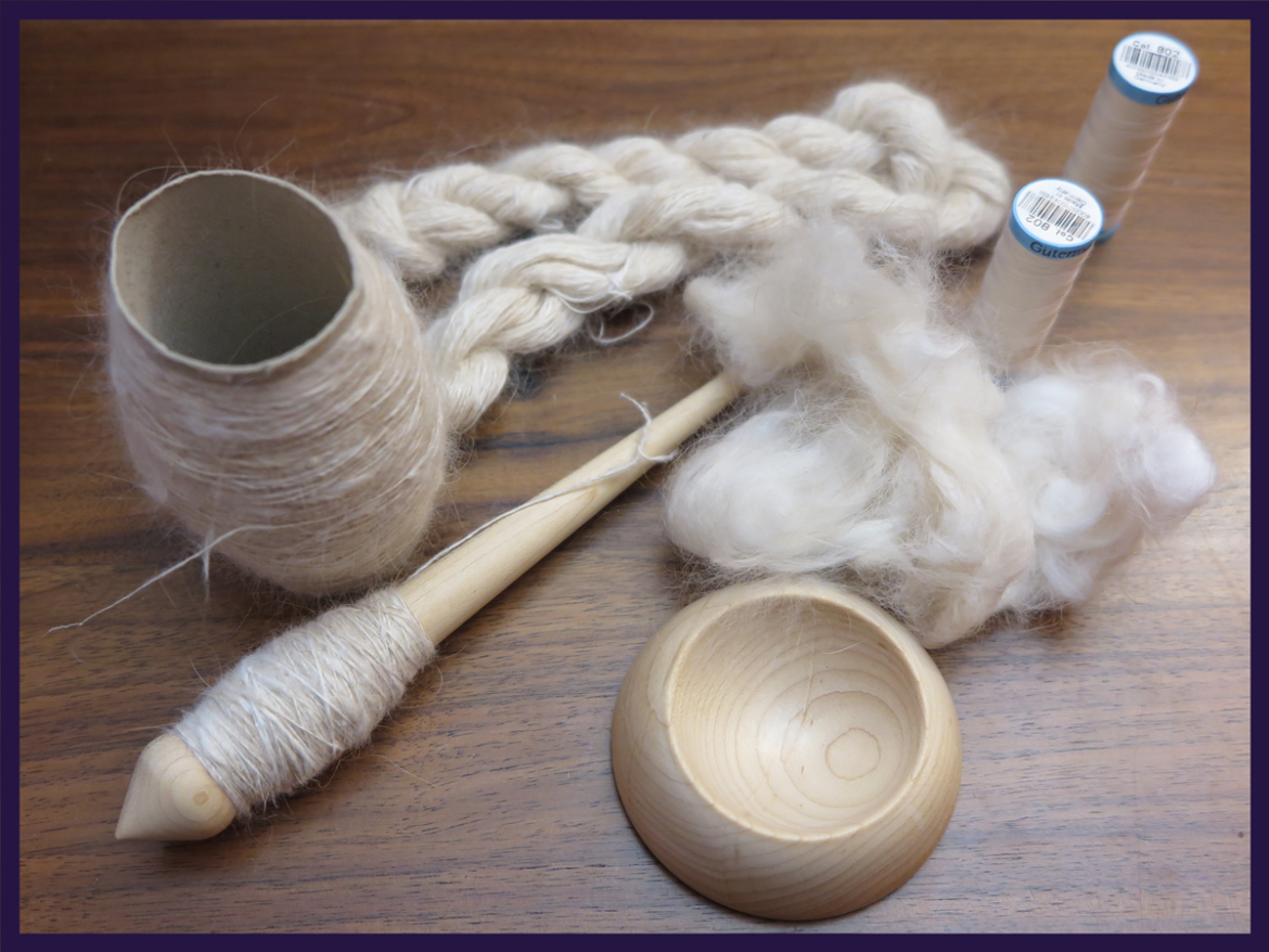 Clockwise from lower left: a pale wood supported spindle with threadlike cream yarn, a toilet paper roll with more of the same yarn, a small skein of plied white yarn, clouds of fawn angora, the matching wood support bowl.