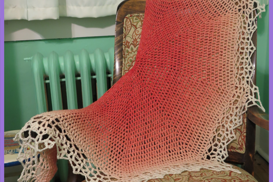 A peach-pink to white gradient crochet lace shawl is draped over a wood rocking chair with a rust red and green paisley pattern. The shawl contrasts with the mint-green paint of the wall behind.