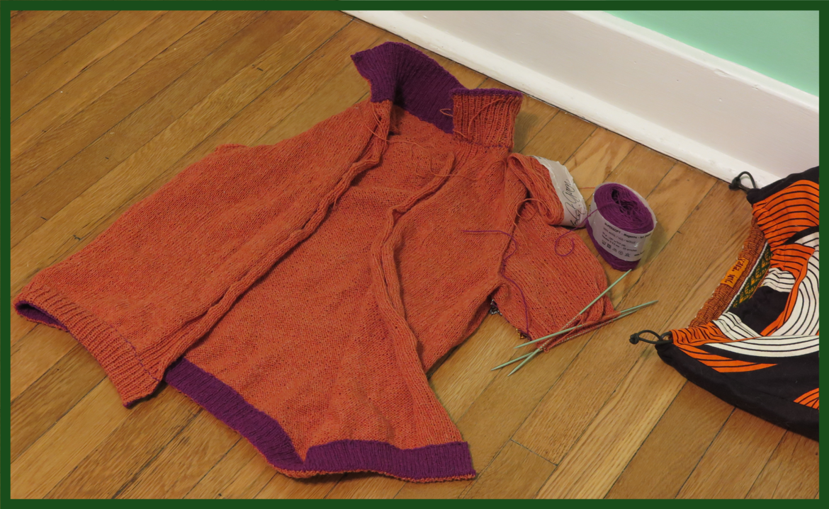 And orange sweater body with purple edging and the beginnings of a sleeve is laid out on a wood floor. The project bag is in the corner and the wall is mint green.