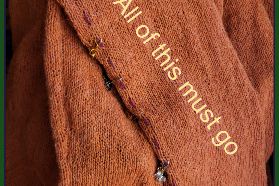 An orange sweater sleeve, not quite finished, with the words "all of this must go" written across it.