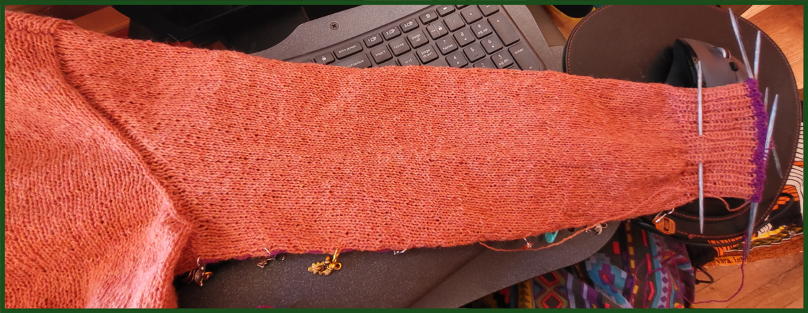 An orange sleeve sweater with DPNs in still in the cuff and stitch markers down the length